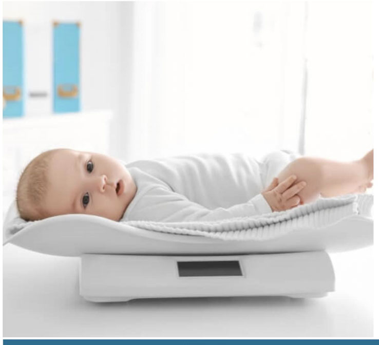 Baby medical scale with a contoured infant tray and a digital display in a clinic setting.