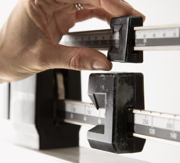 Hand adjusting the sliding weight on a mechanical physician scale for measuring body weight